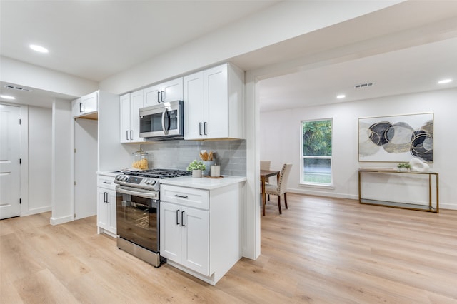 kitchen featuring appliances with stainless steel finishes, white cabinetry, tasteful backsplash, and light wood-type flooring