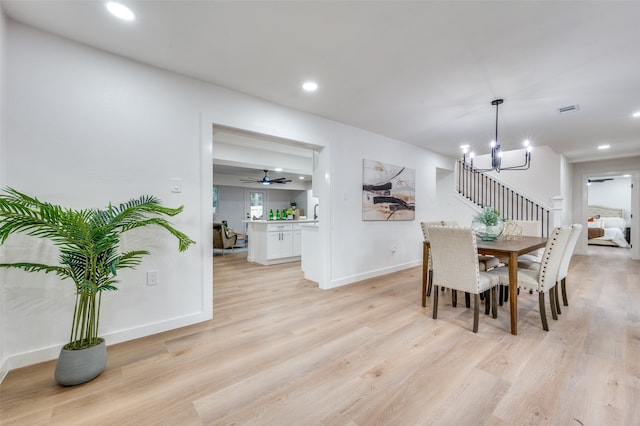 dining room with light hardwood / wood-style floors and ceiling fan with notable chandelier