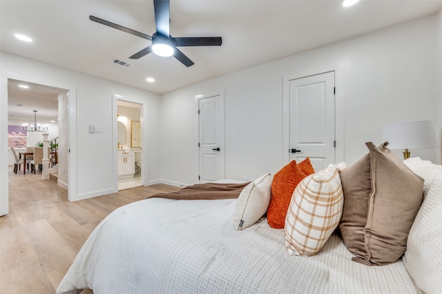 bedroom with light hardwood / wood-style flooring, ensuite bathroom, and ceiling fan with notable chandelier