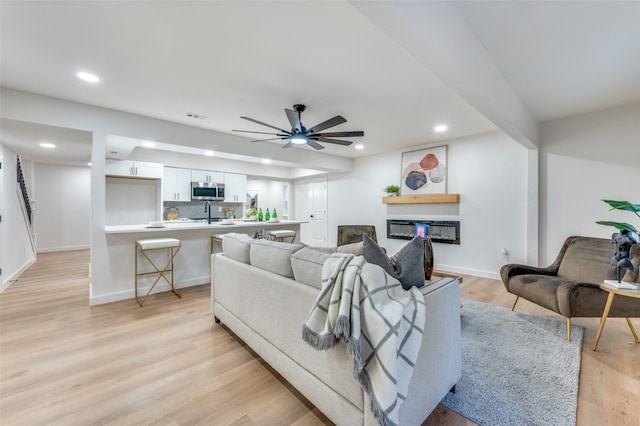 living room featuring ceiling fan, sink, light wood-type flooring, and a fireplace