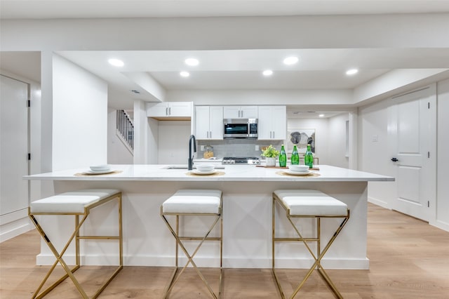 kitchen with a breakfast bar area, an island with sink, stainless steel appliances, light wood-type flooring, and white cabinetry