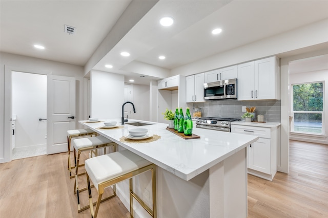 kitchen with appliances with stainless steel finishes, a kitchen island with sink, and white cabinets