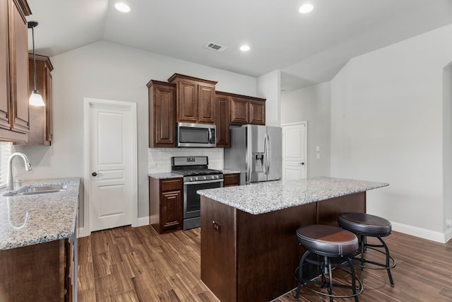 kitchen with dark hardwood / wood-style flooring, appliances with stainless steel finishes, vaulted ceiling, sink, and light stone counters