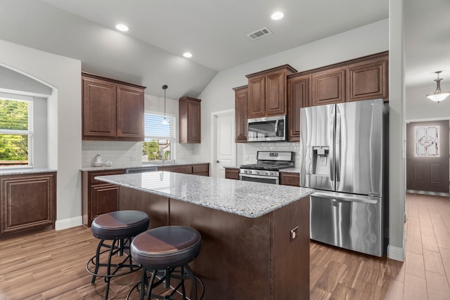 kitchen featuring decorative light fixtures, hardwood / wood-style flooring, stainless steel appliances, and vaulted ceiling