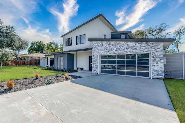 contemporary house featuring stucco siding, concrete driveway, a front yard, fence, and stone siding