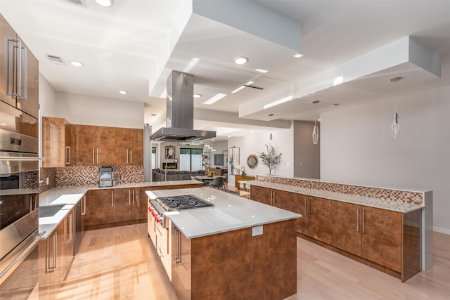 kitchen featuring oven, decorative backsplash, a kitchen island, light wood-type flooring, and island range hood