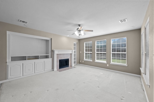 unfurnished living room featuring a textured ceiling, light colored carpet, a tile fireplace, and ceiling fan