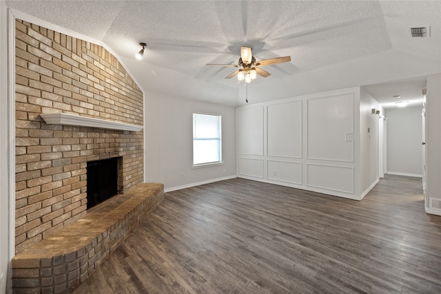 unfurnished living room with a textured ceiling, vaulted ceiling, a brick fireplace, and dark hardwood / wood-style flooring