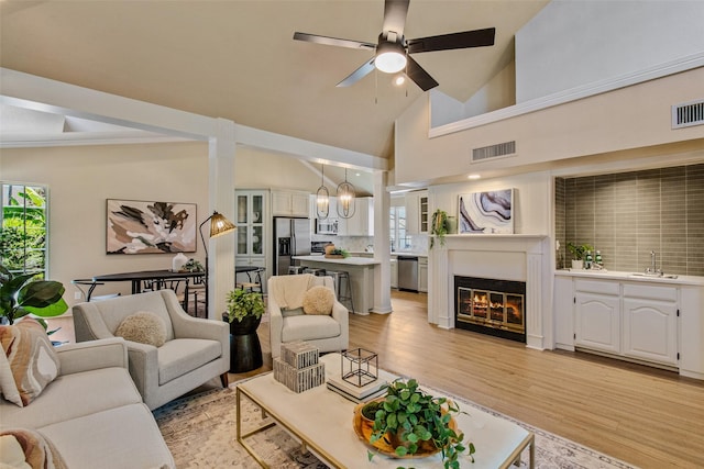 living room featuring ceiling fan with notable chandelier, light hardwood / wood-style floors, high vaulted ceiling, and sink