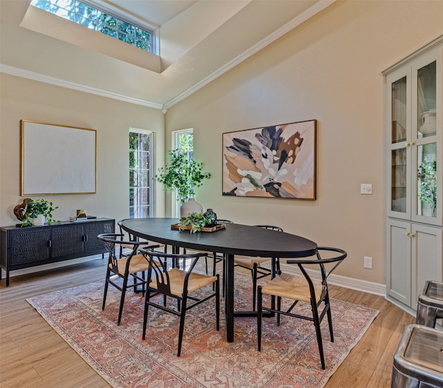 dining area featuring light wood-type flooring, a skylight, high vaulted ceiling, and ornamental molding