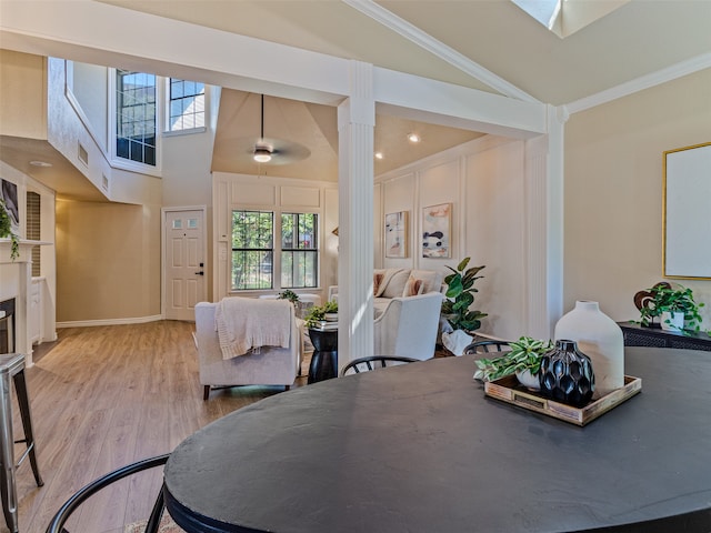 dining area with ceiling fan, high vaulted ceiling, crown molding, a fireplace, and light wood-type flooring