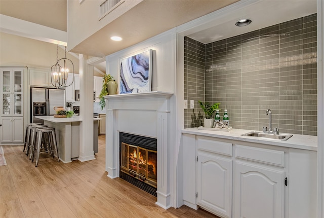 bar featuring sink, light hardwood / wood-style flooring, decorative light fixtures, white cabinetry, and stainless steel fridge with ice dispenser