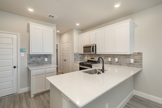 kitchen featuring kitchen peninsula, white cabinets, tasteful backsplash, light hardwood / wood-style flooring, and stainless steel appliances