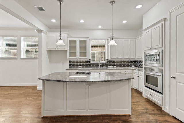 kitchen with stainless steel appliances, a kitchen island, a sink, visible vents, and dark wood finished floors