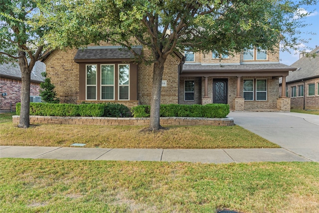 view of front of home with a front lawn, roof with shingles, and brick siding