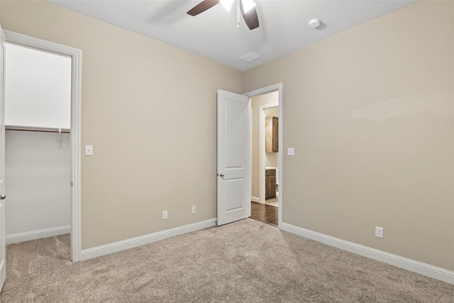 unfurnished bedroom featuring a walk in closet, a closet, light colored carpet, and ceiling fan