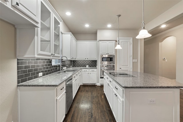 kitchen with dark wood-type flooring, hanging light fixtures, a kitchen island, white cabinetry, and stainless steel appliances