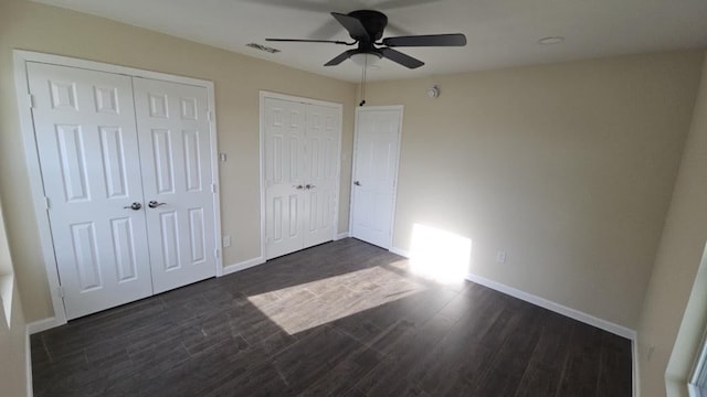 unfurnished bedroom featuring dark wood-style floors, ceiling fan, baseboards, and multiple closets