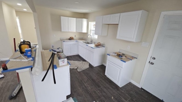 kitchen featuring dark wood-type flooring, white cabinetry, a sink, a peninsula, and baseboards