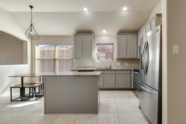 kitchen with stainless steel appliances, backsplash, pendant lighting, gray cabinets, and a kitchen island