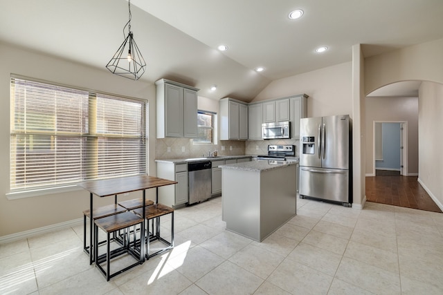 kitchen with appliances with stainless steel finishes, light stone counters, gray cabinets, a kitchen island, and lofted ceiling