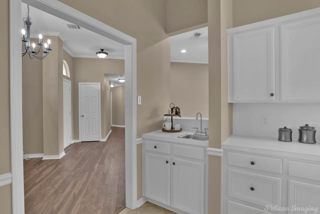 kitchen featuring white cabinets, an inviting chandelier, ornamental molding, light hardwood / wood-style floors, and sink