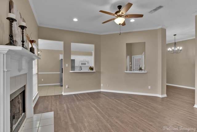 unfurnished living room featuring ceiling fan with notable chandelier, a tile fireplace, sink, crown molding, and light hardwood / wood-style floors