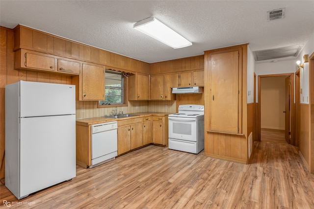 kitchen with sink, light wood-type flooring, a textured ceiling, white appliances, and wood walls