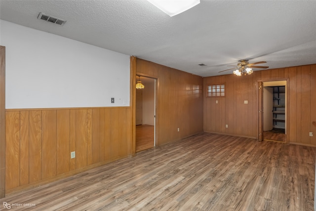 empty room featuring hardwood / wood-style floors, wooden walls, and ceiling fan