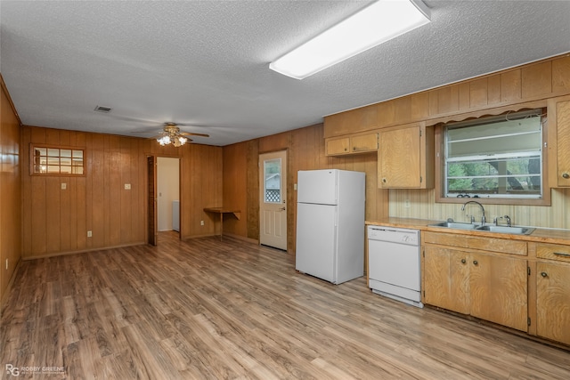 kitchen with white appliances, sink, light wood-type flooring, a textured ceiling, and wooden walls