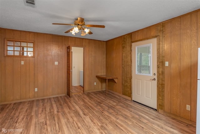 interior space with ceiling fan, a textured ceiling, light wood-type flooring, and wood walls