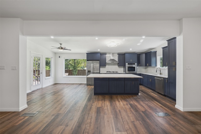 kitchen with wall chimney range hood, stainless steel appliances, sink, and dark hardwood / wood-style flooring