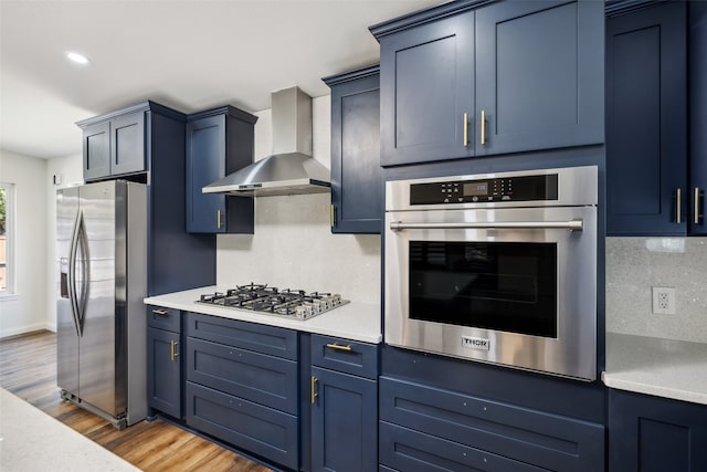 kitchen featuring dark hardwood / wood-style floors, wall chimney exhaust hood, blue cabinetry, appliances with stainless steel finishes, and tasteful backsplash