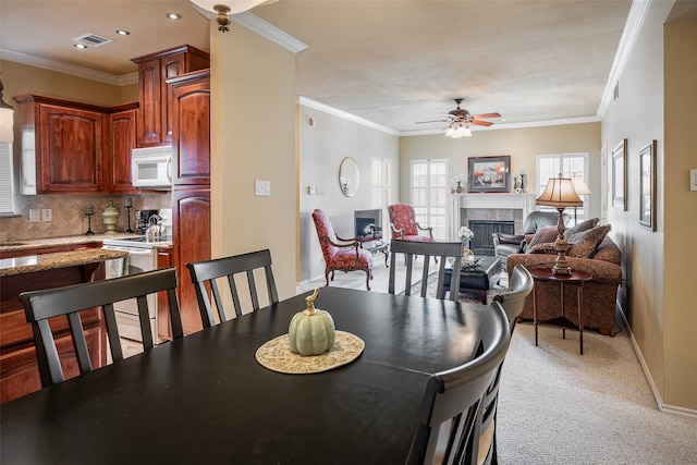 carpeted dining area with ceiling fan and ornamental molding