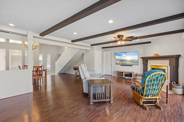 living room featuring a tiled fireplace, beam ceiling, dark hardwood / wood-style flooring, and ceiling fan with notable chandelier