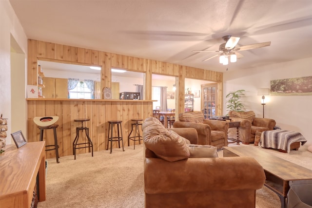 carpeted living room with ceiling fan, wooden walls, and bar area