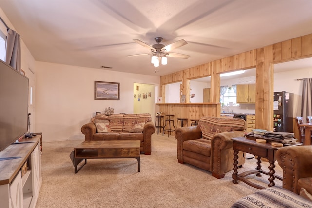 living room with ceiling fan, wood walls, and light colored carpet