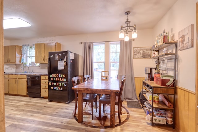 dining space featuring sink, wooden walls, a notable chandelier, and light hardwood / wood-style floors