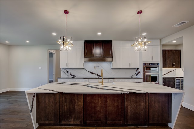 kitchen with a spacious island, stainless steel double oven, light stone countertops, and hanging light fixtures