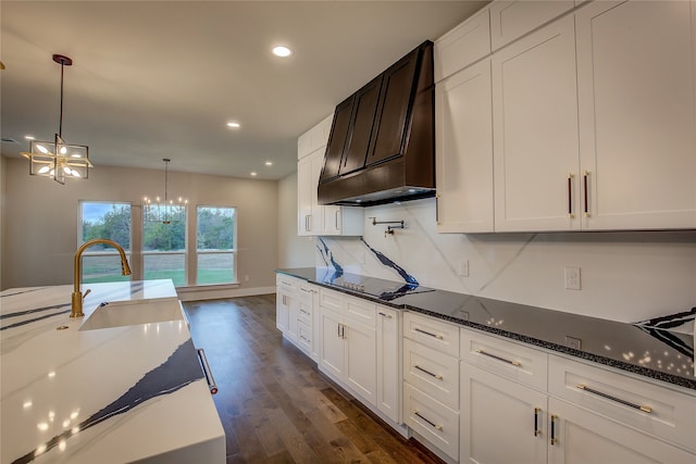 kitchen featuring dark hardwood / wood-style flooring, premium range hood, dark stone countertops, sink, and black stovetop