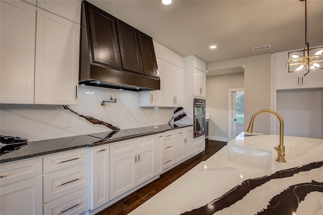 kitchen featuring custom exhaust hood, hanging light fixtures, dark hardwood / wood-style flooring, dark stone countertops, and black electric stovetop