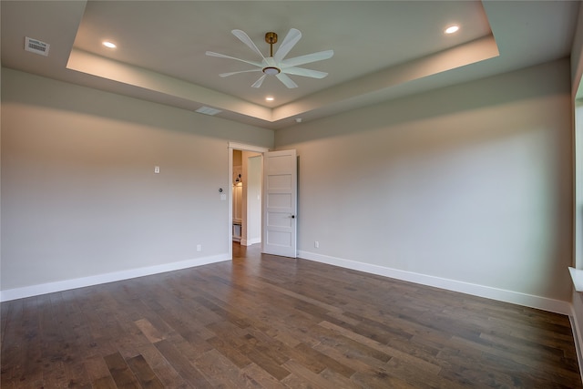 empty room with ceiling fan, a tray ceiling, and dark hardwood / wood-style flooring