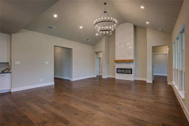 unfurnished living room featuring high vaulted ceiling, dark hardwood / wood-style flooring, a fireplace, and an inviting chandelier