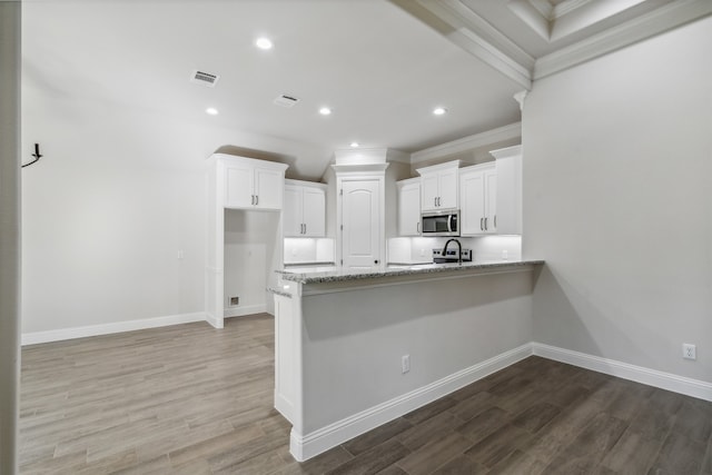 kitchen featuring white cabinetry, light stone countertops, ornamental molding, kitchen peninsula, and hardwood / wood-style flooring