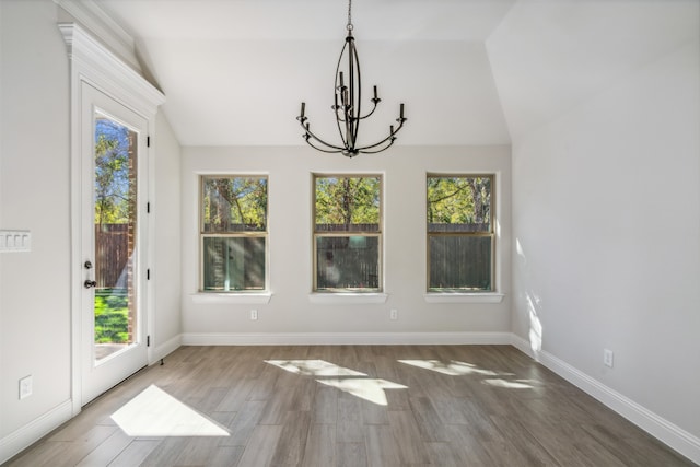 unfurnished dining area featuring a chandelier, dark hardwood / wood-style flooring, a healthy amount of sunlight, and vaulted ceiling