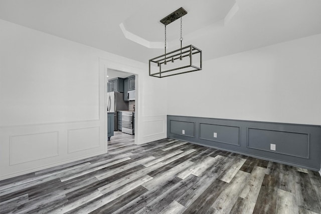 608 N Ave, Whitesboro, TX 76273 - unfurnished dining area with a raised ceiling, dark wood-style floors, a decorative wall, and wainscoting