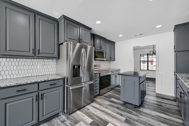 kitchen with decorative backsplash, light stone countertops, dark hardwood / wood-style floors, stainless steel appliances, and a center island