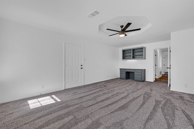 unfurnished living room featuring dark colored carpet, built in desk, and ceiling fan