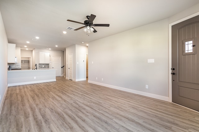 unfurnished living room featuring sink, light wood-type flooring, and ceiling fan