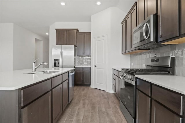 kitchen with sink, dark brown cabinets, light wood-type flooring, stainless steel appliances, and backsplash